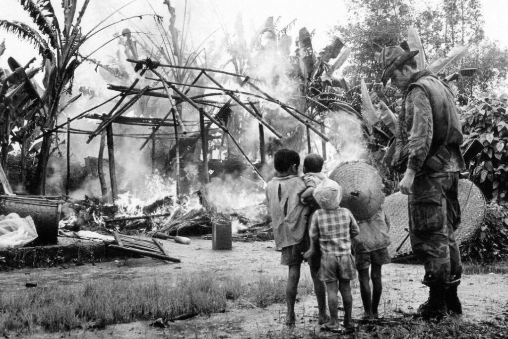 USA soldier and Vietnamese children look on how their village is burned down 