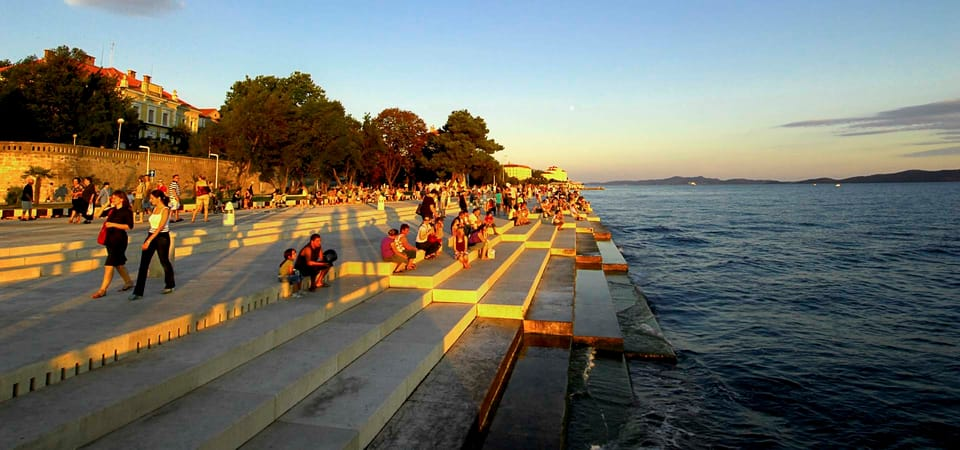 People sitting on the marble steps of the quay. The holes in the steps are responsible for the tune produced by the sea.