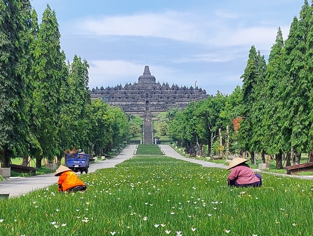 Overview of the main temple of the Borobudur Temple Complex near Yogyakarta. In the forefront two women tending the flower beds.